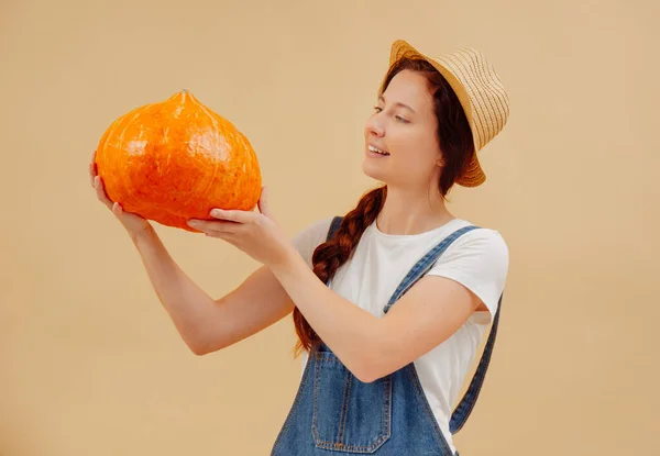Female gardener looks at a ripe organic pumpkin on yellow background. — Stock Photo, Image
