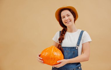 Kadın bahçıvan bej arka planda olgun bir balkabağı tutuyor..