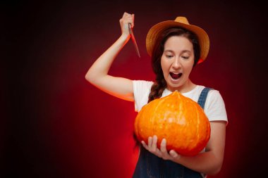 Bahçıvan kadın olgun bir balkabağına kırmızı arka planda bıçakla saldırıyor.