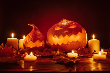 Kırmızı arka planda korkunç oyulmuş yüzleri olan balkabakları mumlarla aydınlatılıyor.