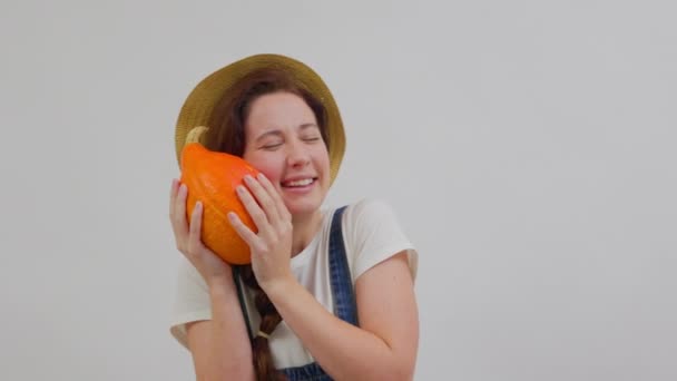 Campesina vestida con overoles y un sombrero abraza una calabaza naranja madura. — Vídeos de Stock