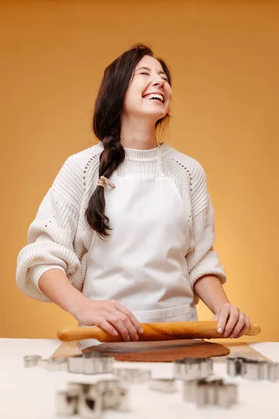 Kadın pastacı gülerek hamuru oklavayla yuvarlıyor..
