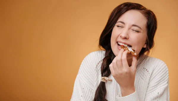 Woman biting a gingerbread Christmas cookie on a yellow background. — Stock Photo, Image