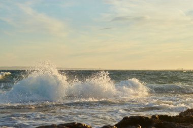 Gün batımında dalgalar kayalık sahile çarpıyor.