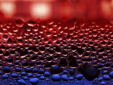 Transparent water drops on window. Red and blue tint. Condensate close up.