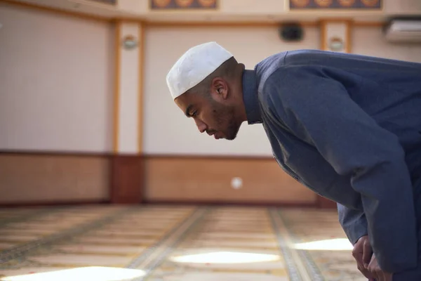 Вид сбоку на молодого мусульманина, кланяющегося во время молитвы в мечети — стоковое фото