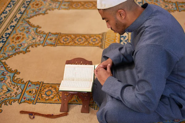 Πλευρική άποψη ενός νεαρού μουσουλμάνου άνδρα που διαβάζει το Κοράνι μέσα σε ένα τζαμί — Φωτογραφία Αρχείου