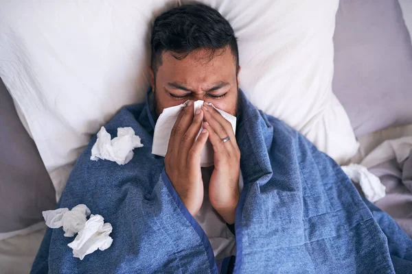 En bild av en sjuk man som blåser sig i näsan när han ligger i sängen — Stockfoto