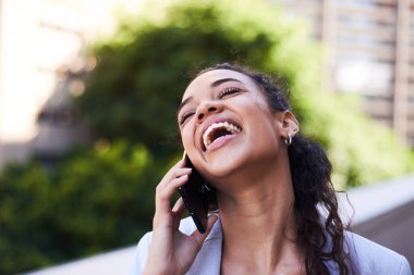 Genç bir kadın cep telefonuyla konuşurken mutlu bir şekilde güler.