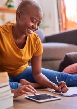 Genç bir öğrenci yerde oturup kitap ve tabletle ders çalışıyor.