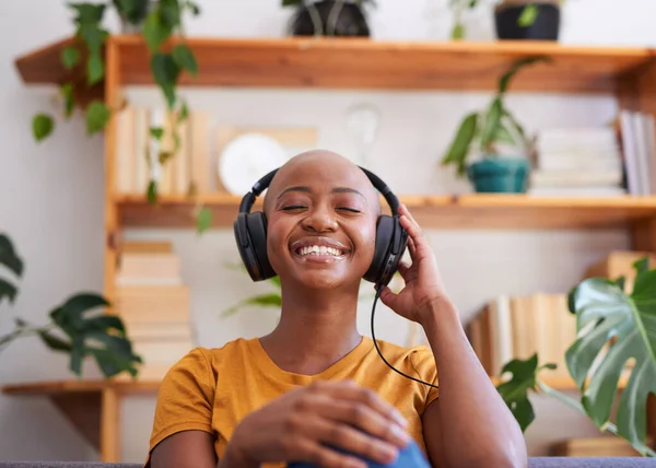 Genç bir kadın oturma odasındaki kanepede kulaklıkla müzik dinliyor.
