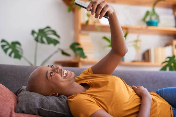 Μια νεαρή γυναίκα ξαπλώνει στον καναπέ και κοιτάζει το κινητό της. — Φωτογραφία Αρχείου