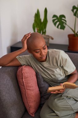 Genç bir kadın evinde kanepede roman okuyor.