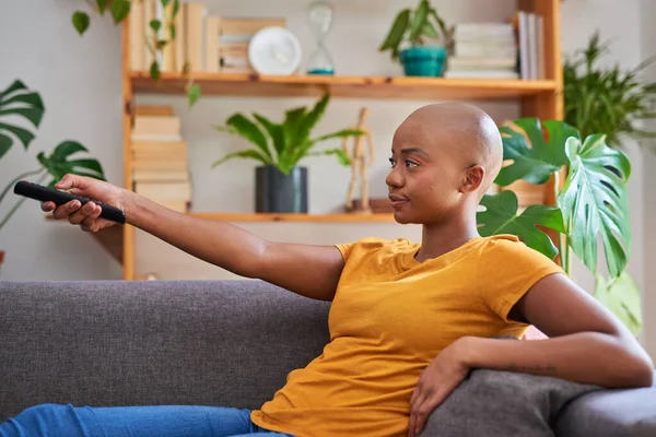 Μια νεαρή γυναίκα δείχνει το τηλεκοντρόλ στην τηλεόραση καθισμένη στον καναπέ χαλαρώνοντας — Φωτογραφία Αρχείου