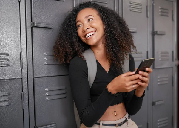 Eine junge Studentin mit gemischter Rasse lacht, als sie im College vor Schließfächern textet — Stockfoto
