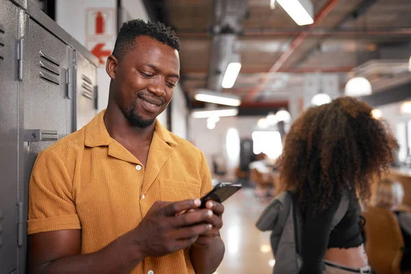 Ein junger schwarzer Student schaut auf sein Handy, während eine Frau auf dem Campus vorbeiläuft — Stockfoto