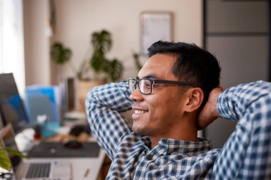 Genç bir ofis çalışanı sırasına yaslanıp gözlük takıyor.