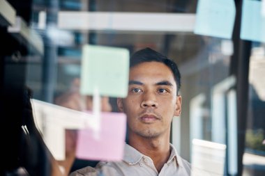 Asyalı bir adam pencereden görüldüğü gibi yapışkan notlarla beyin fırtınası yapar.