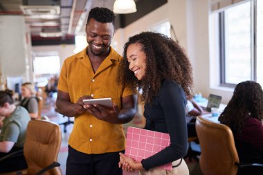 Two colleagues look at digital tablet in open plan diverse office