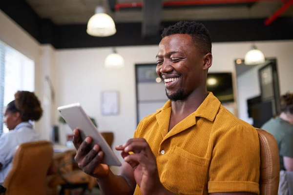 Um homem negro usa um tablet digital no escritório em plano aberto usando camisa brilhante — Fotografia de Stock
