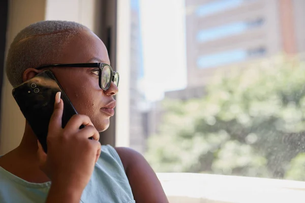 A young Black businesswoman takes a call while looking out the office window — Stockfoto