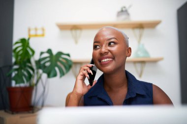 Genç siyahi bir iş kadını ofisteki bir cep telefonuna gülümsüyor.