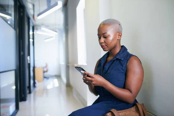 한 흑인 여성 이 사무실 복도에서 앉아서 기다리면서 문자를 보내는 모습 — 스톡 사진