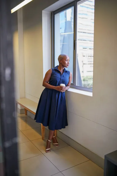 A young Black businesswoman looks out the window in city office on coffee break — Stockfoto