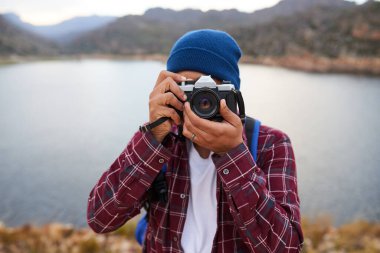 Tanımlanamayan bir adam gölle dağlarda yürüyüş yaparken klasik kamera kullanarak fotoğraf çekiyor. Yüksek kalite fotoğraf
