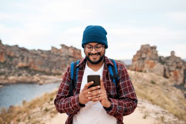 Çekici bir adam kayalık yabanda yürürken akıllı telefonuna gülümser. Yüksek kalite fotoğraf
