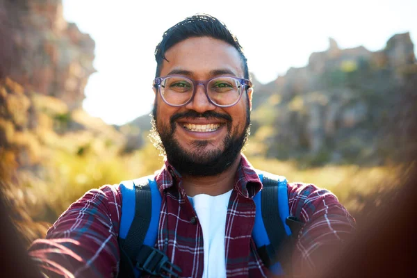 A South Asian adult man takes a selfie while hiking in the mountains. High quality photo