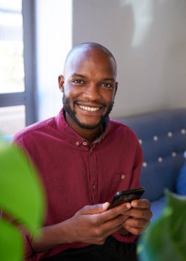 Çekici bir siyah adam telefonunu kullanırken kameraya gülümsüyor. Yüksek kalite fotoğraf