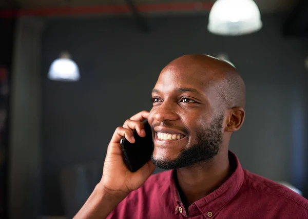 A Black man smiles on a cellphone call in the office. High quality photo
