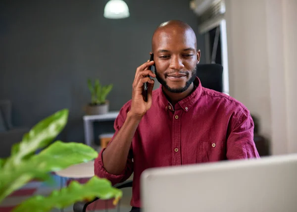 A Black businessman looks at his screen while answering call in the office. High quality photo