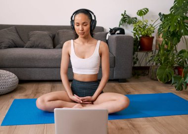 A young woman listens to guided meditation on her yoga mat at home with cat. High quality photo