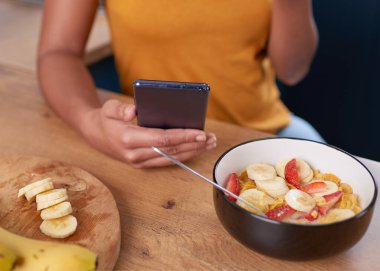 A young woman looks at her cellphone while eating healthy breakfast. High quality photo