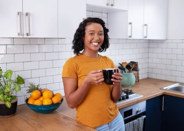 A young multi-ethnic woman relaxes in clean kitchen with mug of coffee. High quality photo