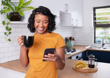 A young multi-ethnic woman laughs and looks at her phone in the kitchen. High quality photo