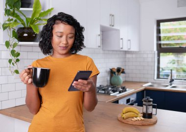 A young multi-ethnic woman reads a message on her phone at breakfast. High quality photo