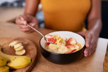 A close up of young woman eating bowl of cornflakes with fruit for breakfast. High quality photo