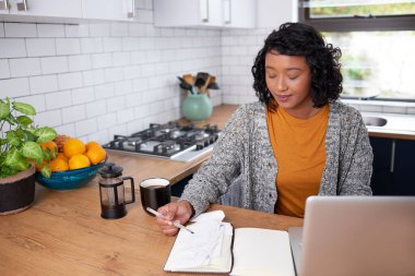 A young multi-ethnic woman reviews her household finances in the kitchen. High quality photo