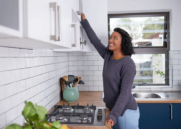 A young multi-ethnic woman reaches into her kitchen cupboards. High quality photo