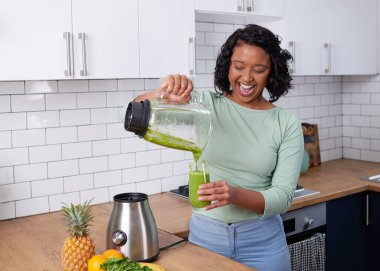 A young multi-ethnic woman pours a fresh green smoothie from blender in kitchen. High quality photo