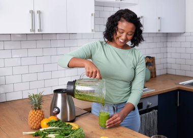 A young multi-ethnic woman pours a fresh green smoothie from blender in kitchen. High quality photo