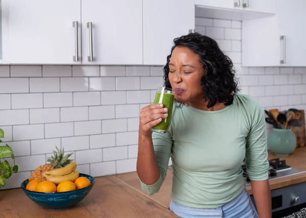 A young multiracial woman forces herself to drink a nasty tasting green smoothie. High quality photo