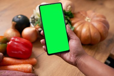 Close up of mobile phone screen with whole vegetables on kitchen counter. High quality photo