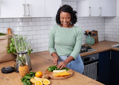 A young multiracial woman chops fruit and spinach for green smoothie. High quality photo