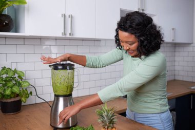 A young multi-ethnic woman blends a smoothie on kitchen counter. High quality photo