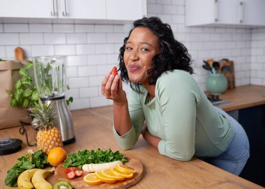 A young attractive woman tastes a strawberry while preparing fruit for smoothie. High quality photo