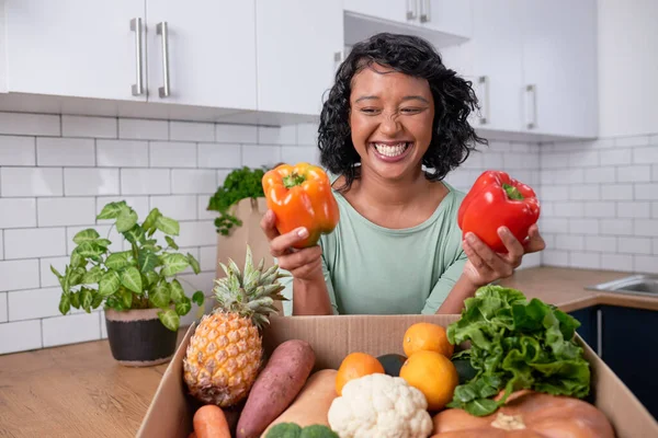 A young multi-ethnic woman holds two sweet peppers out of fresh veg delivery box. High quality photo